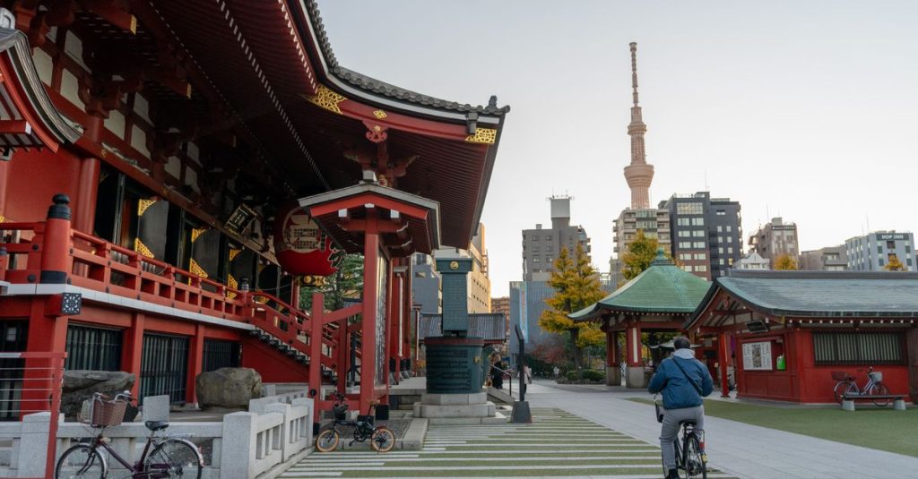 Bâtiments rouges d'un temple d'Asakusa, avec la Tokyo Skytree en arrière-plan et un cycliste