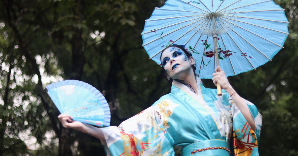 Woman in a turquoise kimono with stage make-up, holding a parasol and blue fan