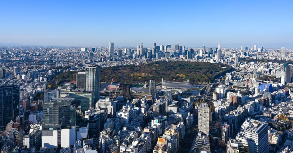 Vue aérienne d'une grande ville japonaise par temps clair, avec ses immeubles et un vaste parc boisé