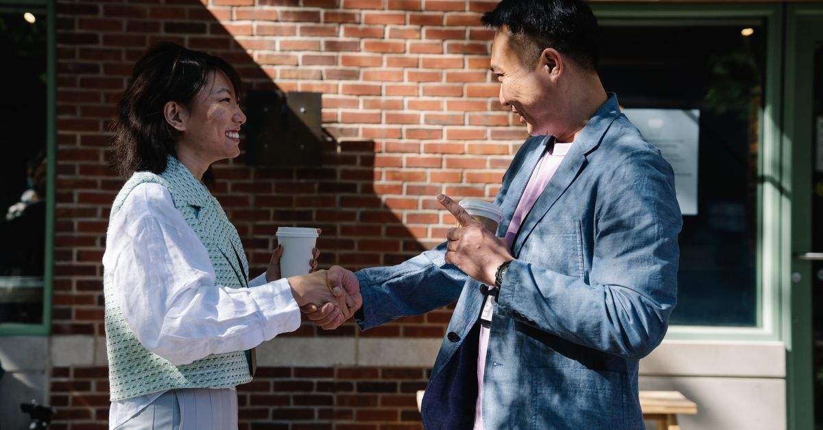 Two smiling people shaking hands in front of a brick wall