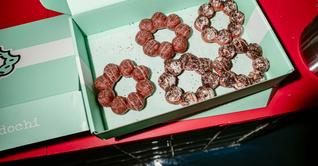 Boîte de beignets en anneau garnis de glaçage et de poudre, type « mochi donuts », sur fond rouge