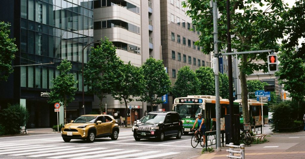 Carrefour bordé d'arbres et d'immeubles de bureaux, avec bus et voitures