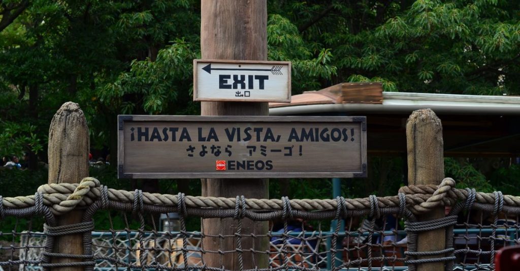 Panneau de sortie en espagnol et en japonais (« Hasta la vista, amigos ! ») dans un parc Disney, au milieu de la végétation